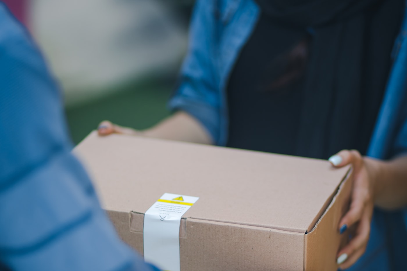A plain, sealed cardboard box being handed from a delivery driver to a customer